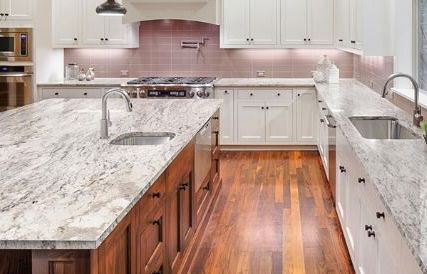 Bright modern kitchen with white cabinets, pink backsplash, and marble islands with wood flooring