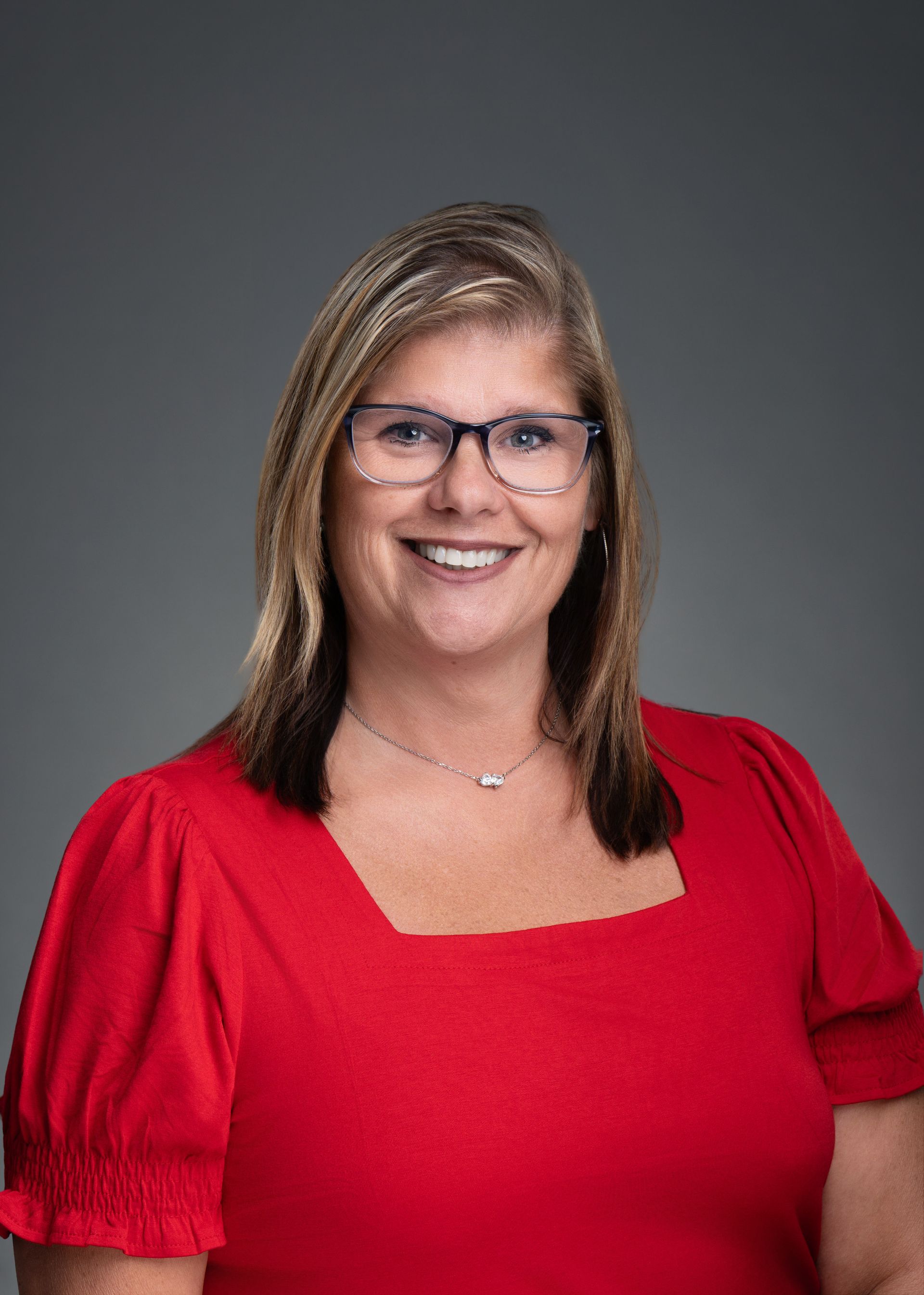 Woman in a red top and glasses smiling against a gray background
