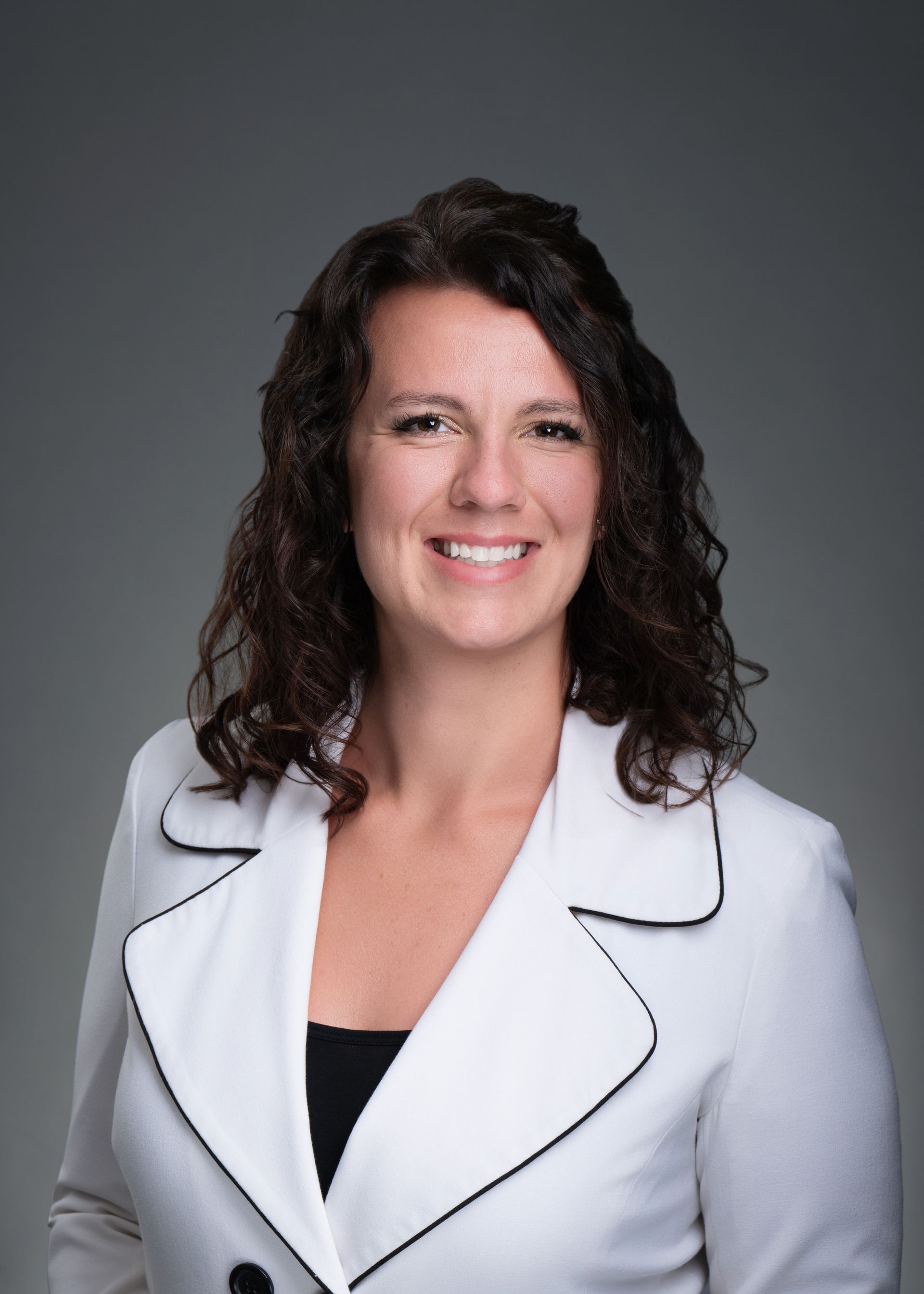 Smiling person with curly dark hair in a teal dress against a gray studio background