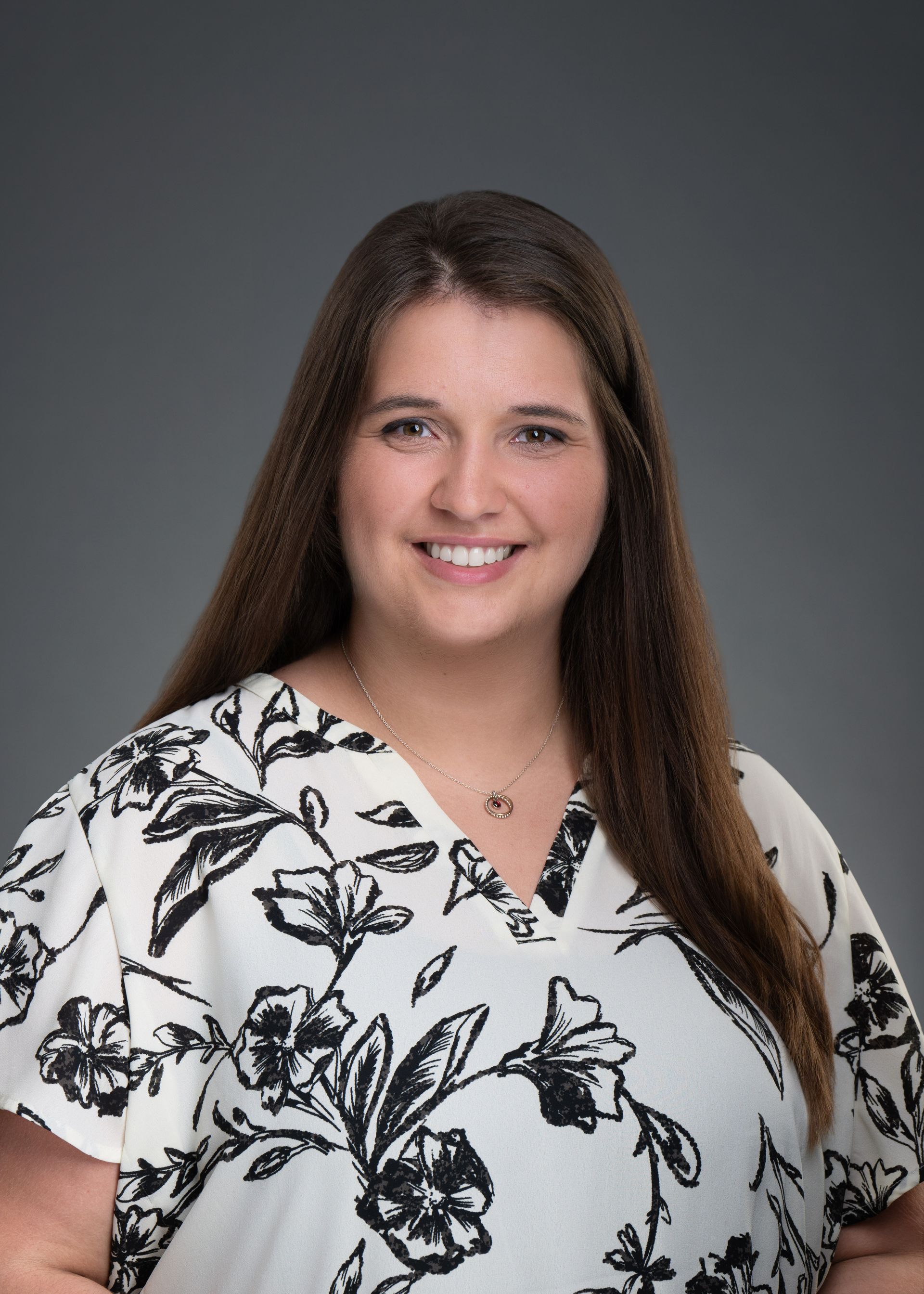 Studio portrait of a smiling woman in a white floral blouse against a gray background