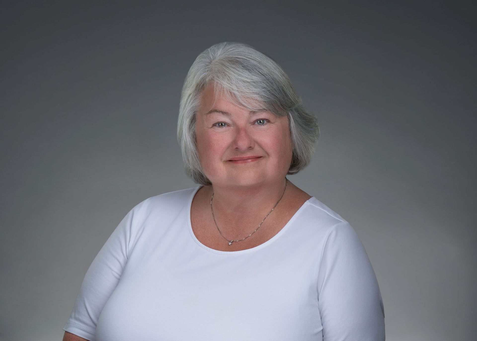 Smiling person in a white top against a gray studio background