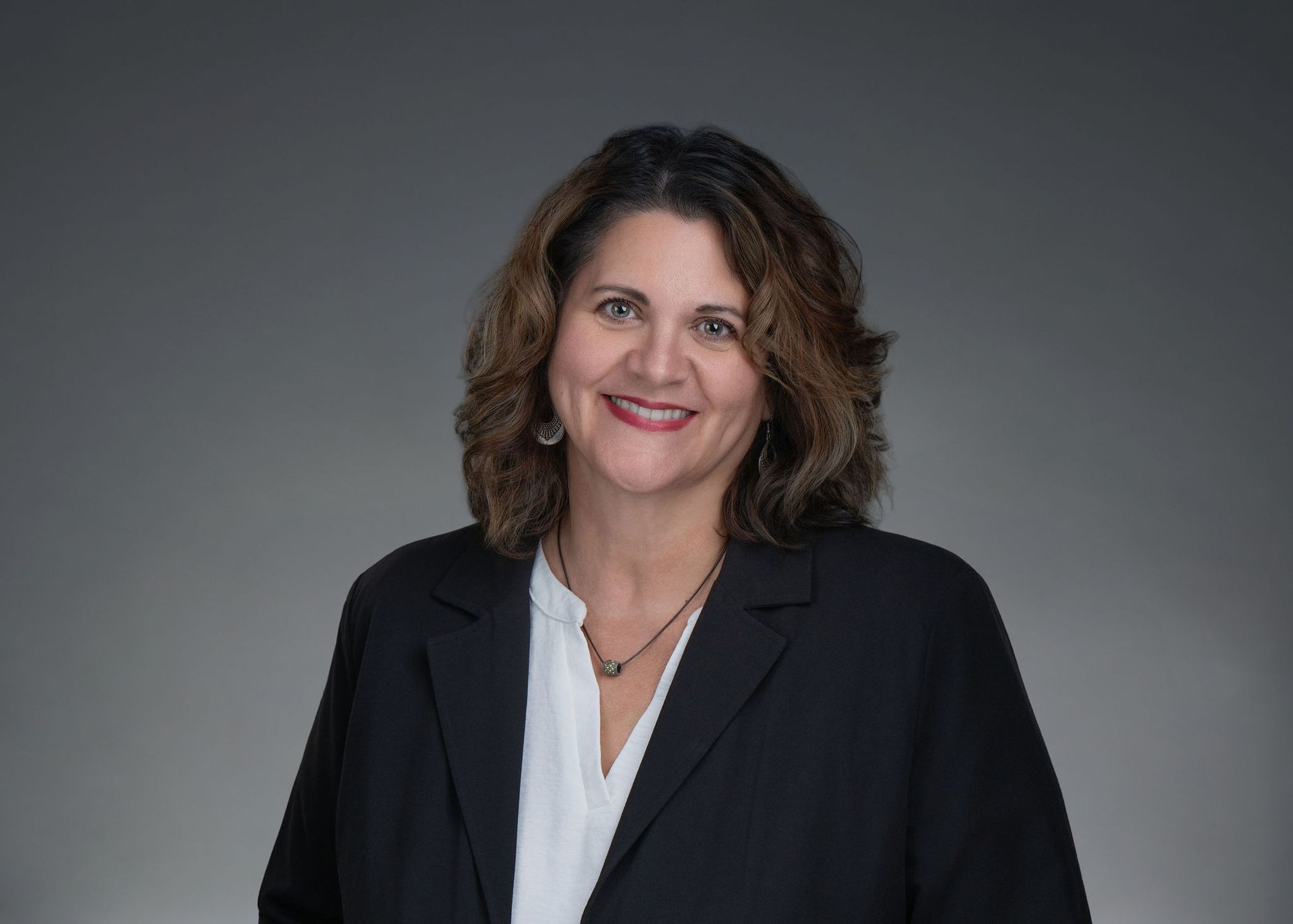 Smiling woman in a black blazer and white blouse against a gray background