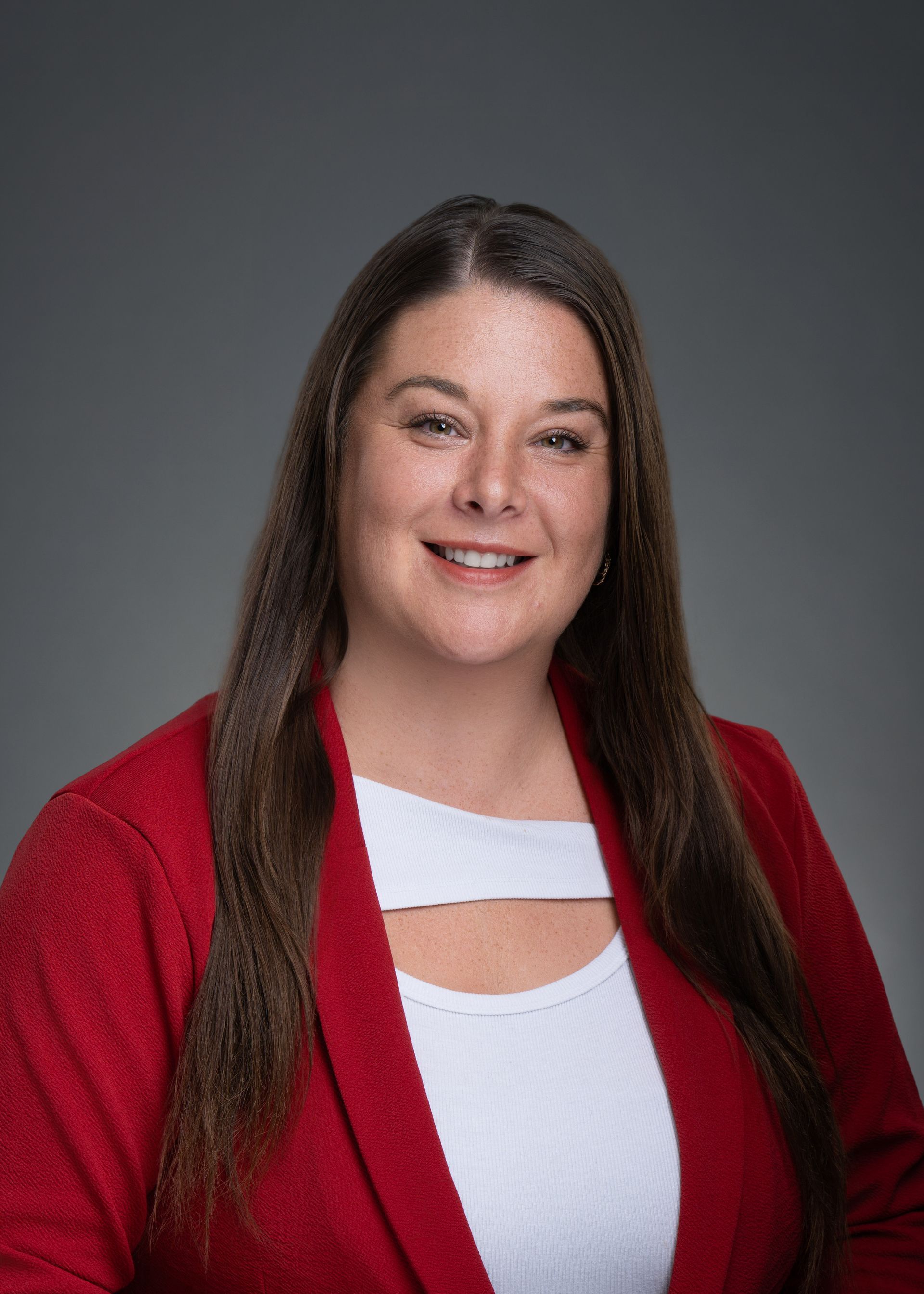 Woman in a red cardigan and white top, smiling against a gray studio background