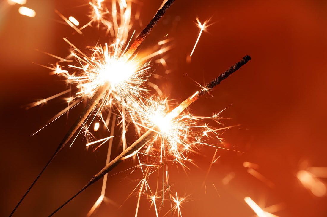 Two sparklers burning with bright white sparks against a warm orange background
