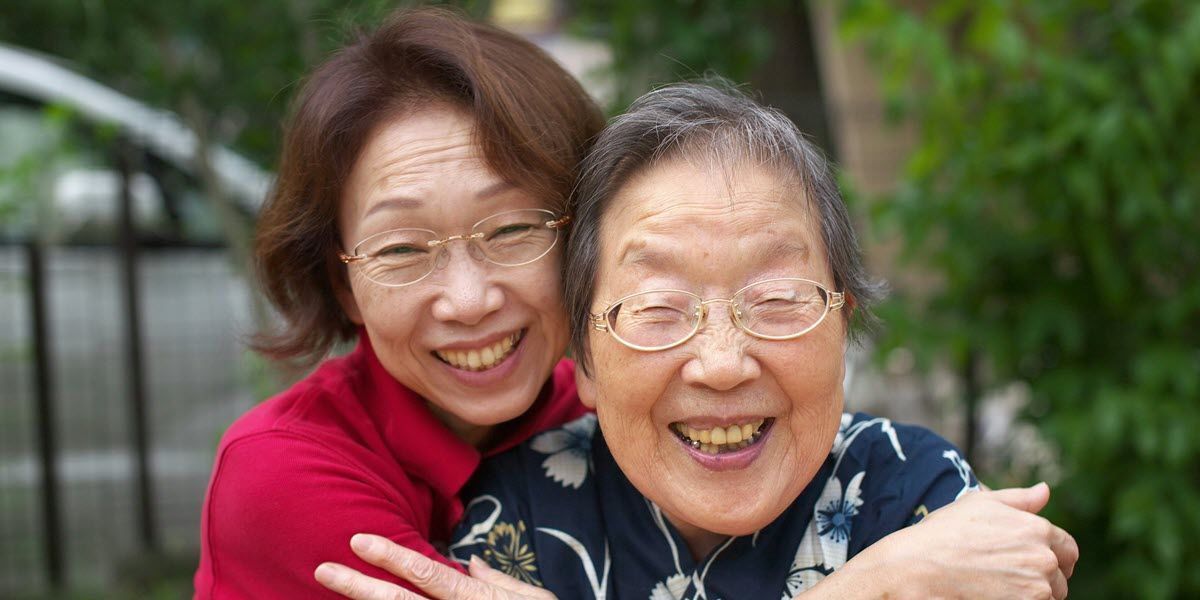 Two smiling women hugging outdoors, one in a red sweater and the other in a navy floral top.