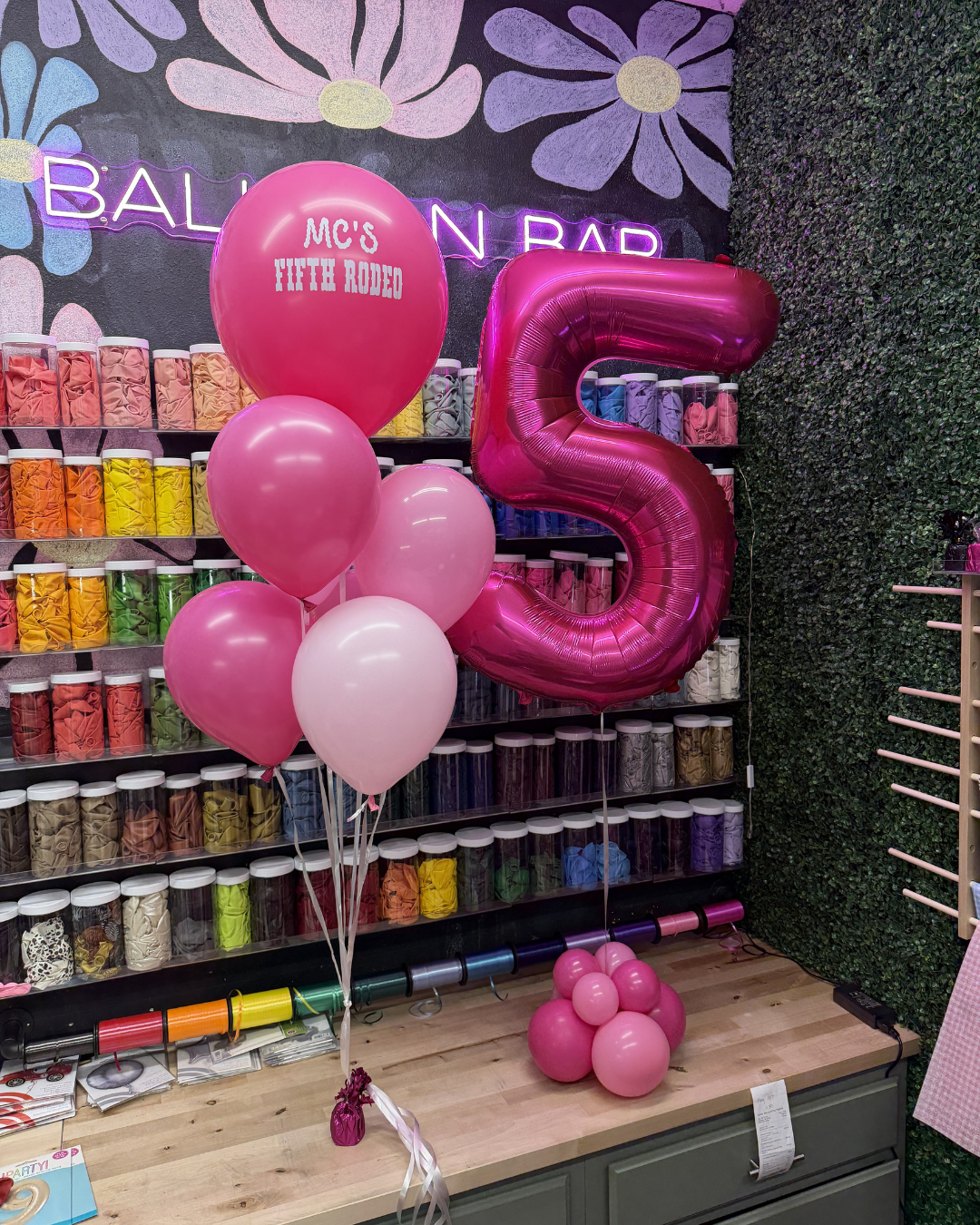 Pink balloon display with a large metallic “5” at a balloon shop backdrop