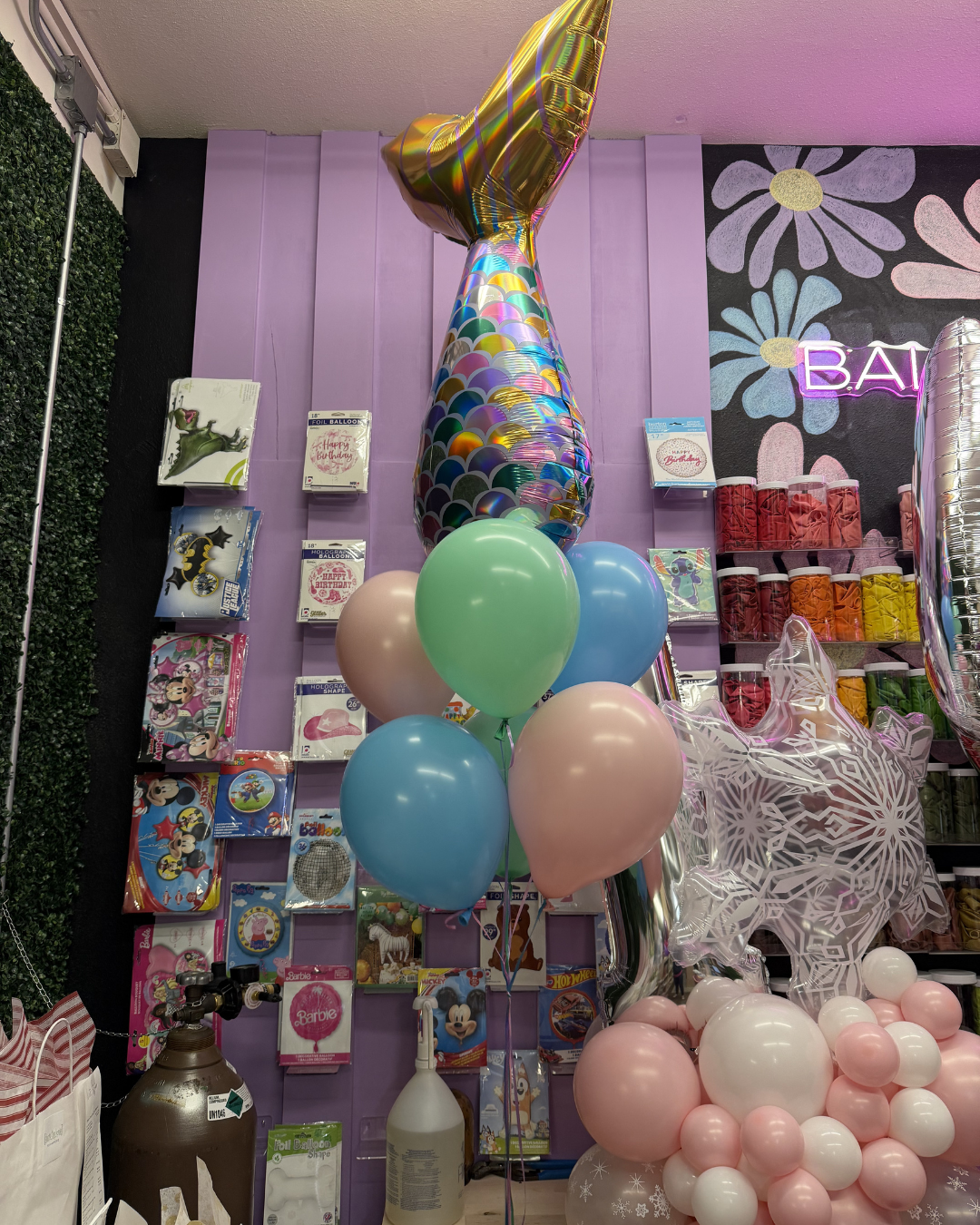 Balloon display with pastel pink, blue, and green balloons in a colorful party shop with gift boxes and decor.