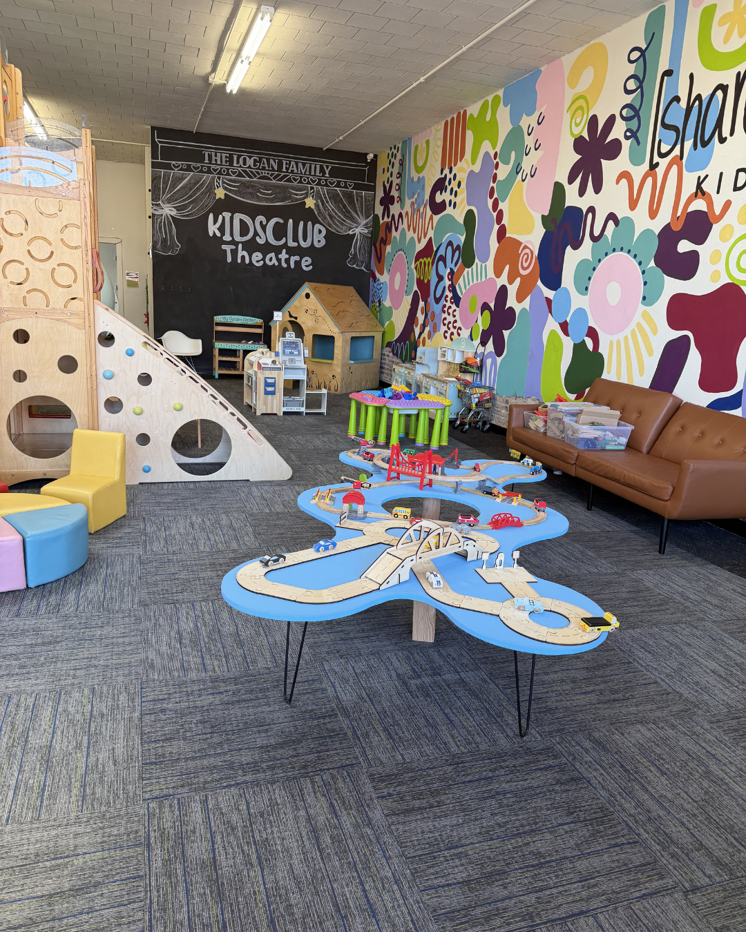 Colorful kids’ playroom with mural wall, carpet, play tables, climbing structure, and couch