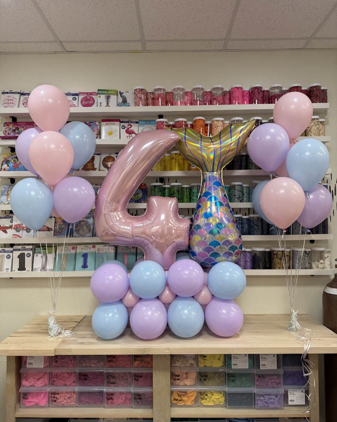 Pastel balloon arrangement with a large pink 4 and confetti balloon in a shop display.