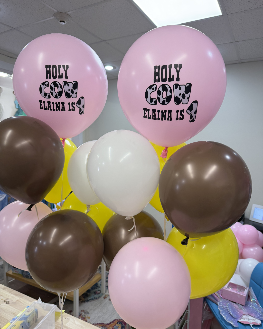 Pink, brown, white, and yellow balloons with “Holy” text, decorating an indoor room.