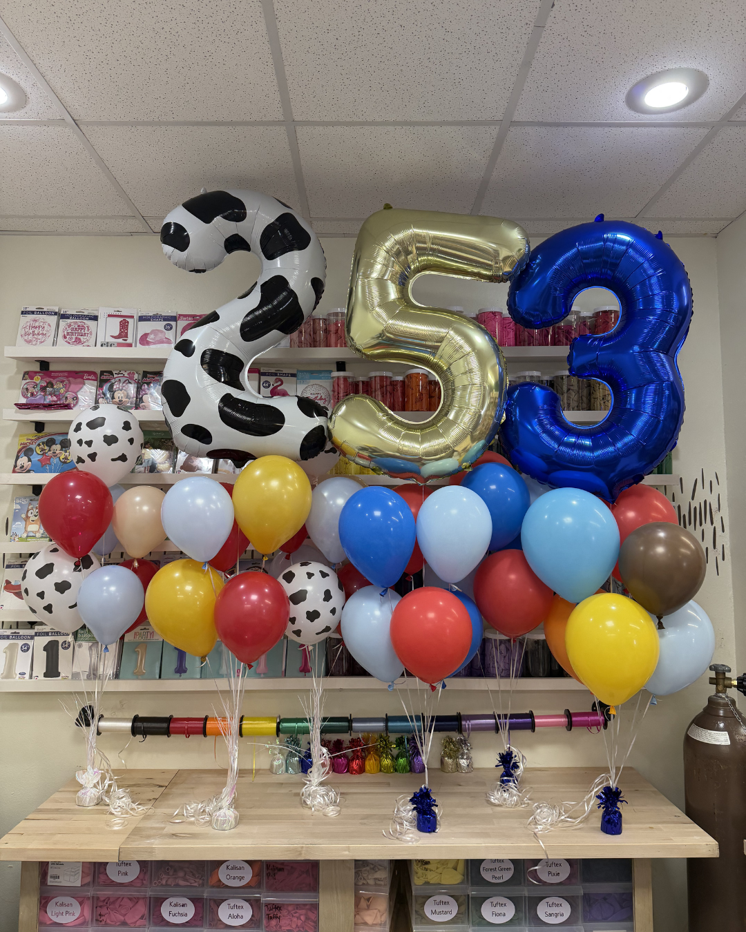 53 balloon display with a gold 5, blue 3, and black-and-white cow-print 2 above colorful balloons