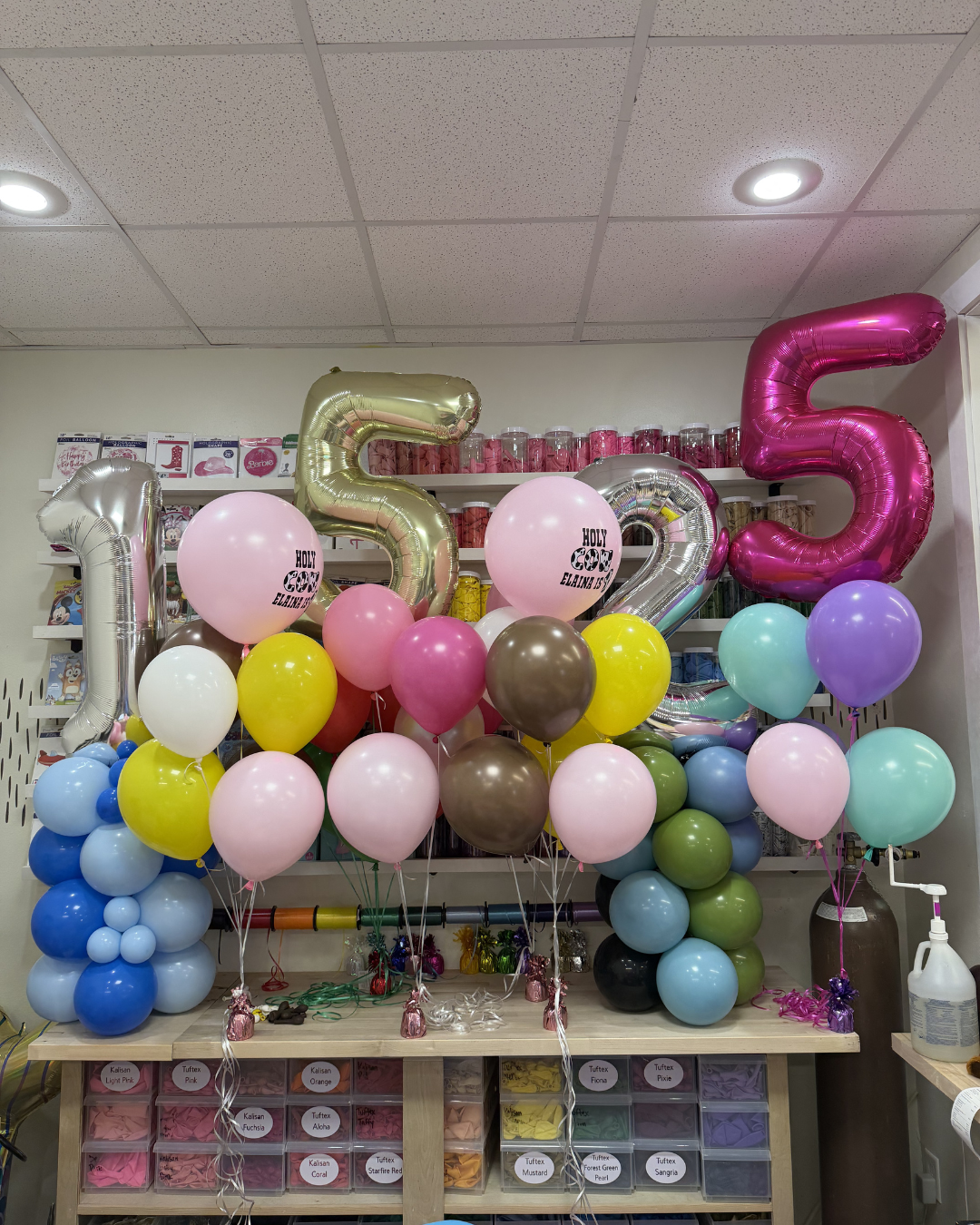 Colorful balloon display with large metallic 1, 5, 2, 5 numbers above a dessert counter in a party room