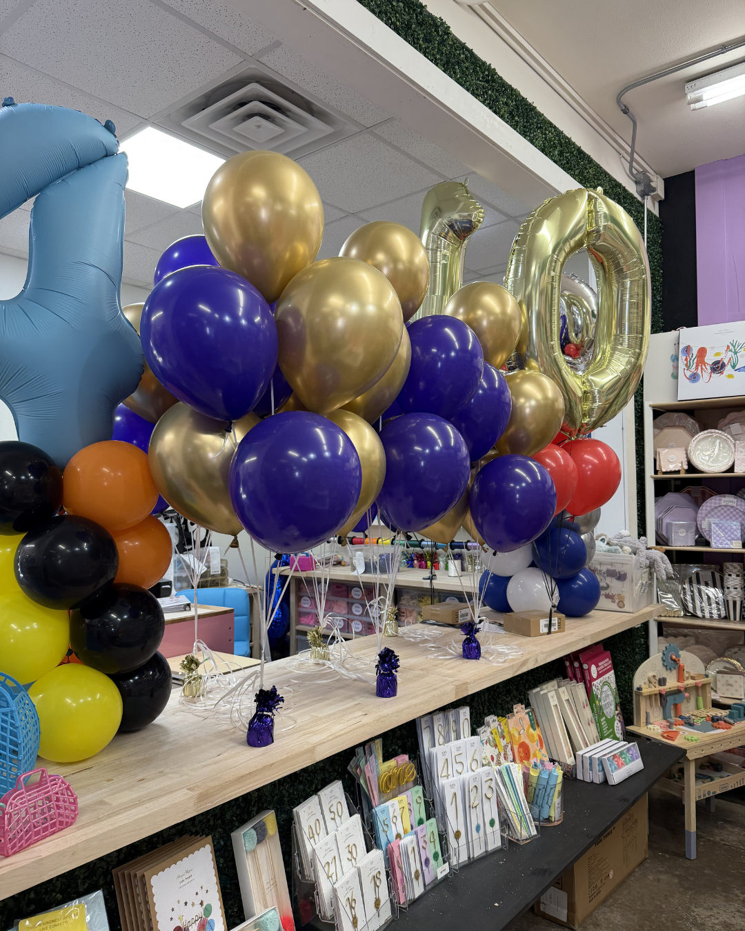 Balloon display with gold, purple, blue, and black balloons in a party store aisle