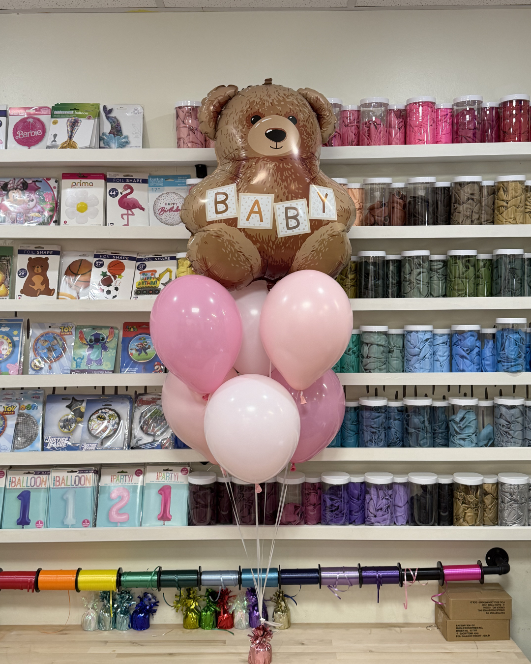Teddy bear centerpiece with BABY blocks and pink balloons in a party supply store