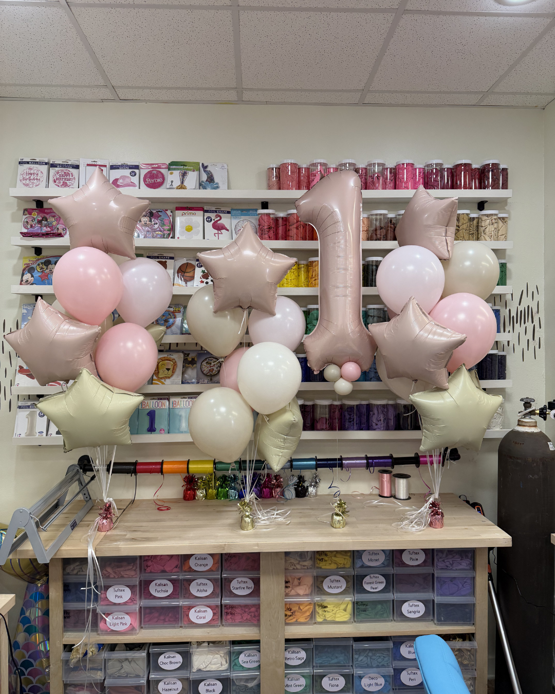 Balloon-decorated dessert shop counter with pink, white, and gold balloons, including a large “1” centerpiece