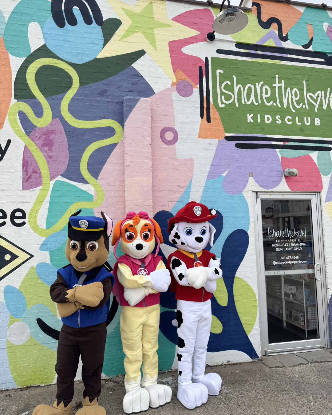Three Paw Patrol mascots pose outside a colorful storefront mural.