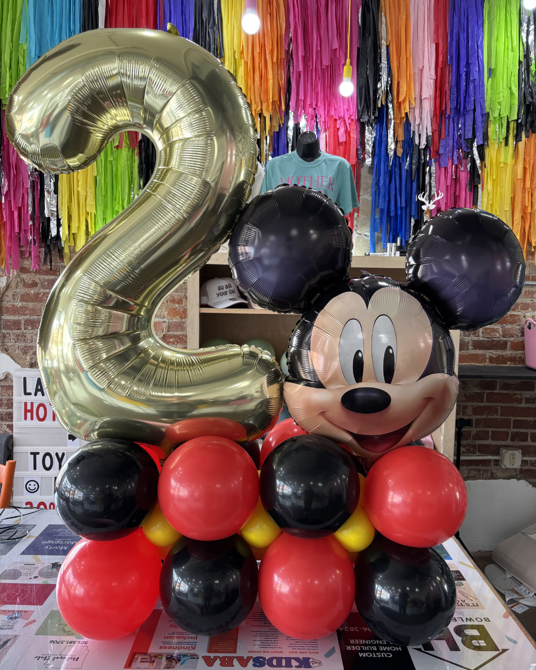 Mickey Mouse balloon display with a gold number 2 balloon and black, red, and gold balloons at a party backdrop