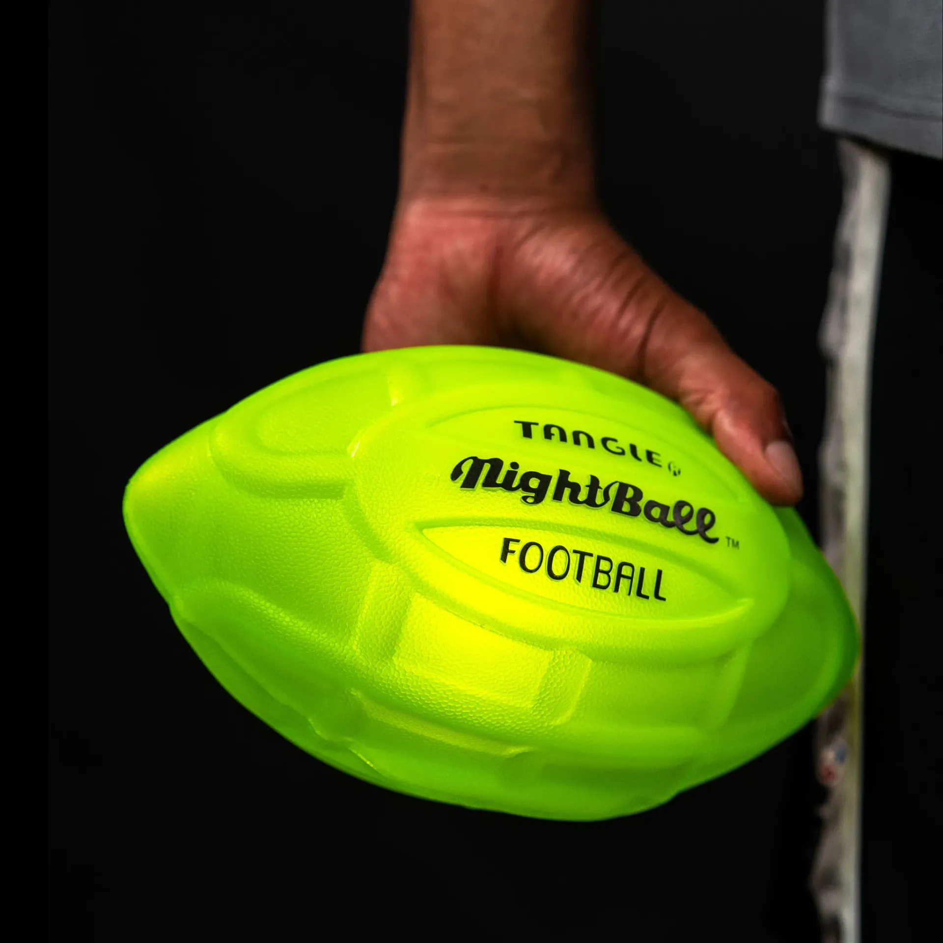 Hand holding a neon green football with black text on a dark background