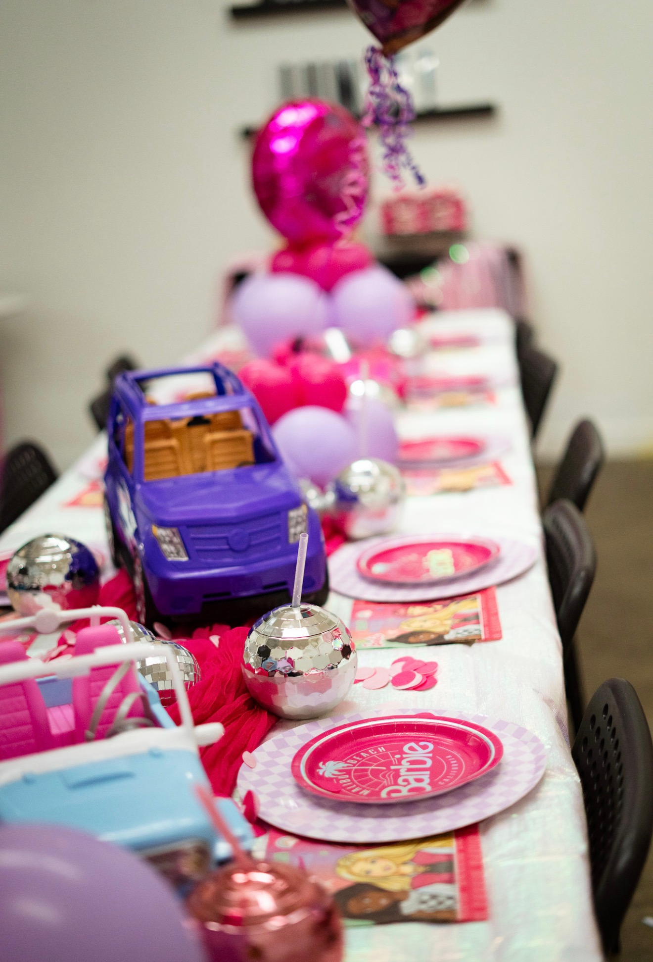 Decorated table with pink balloons, toy purple truck, and pink-themed party place settings