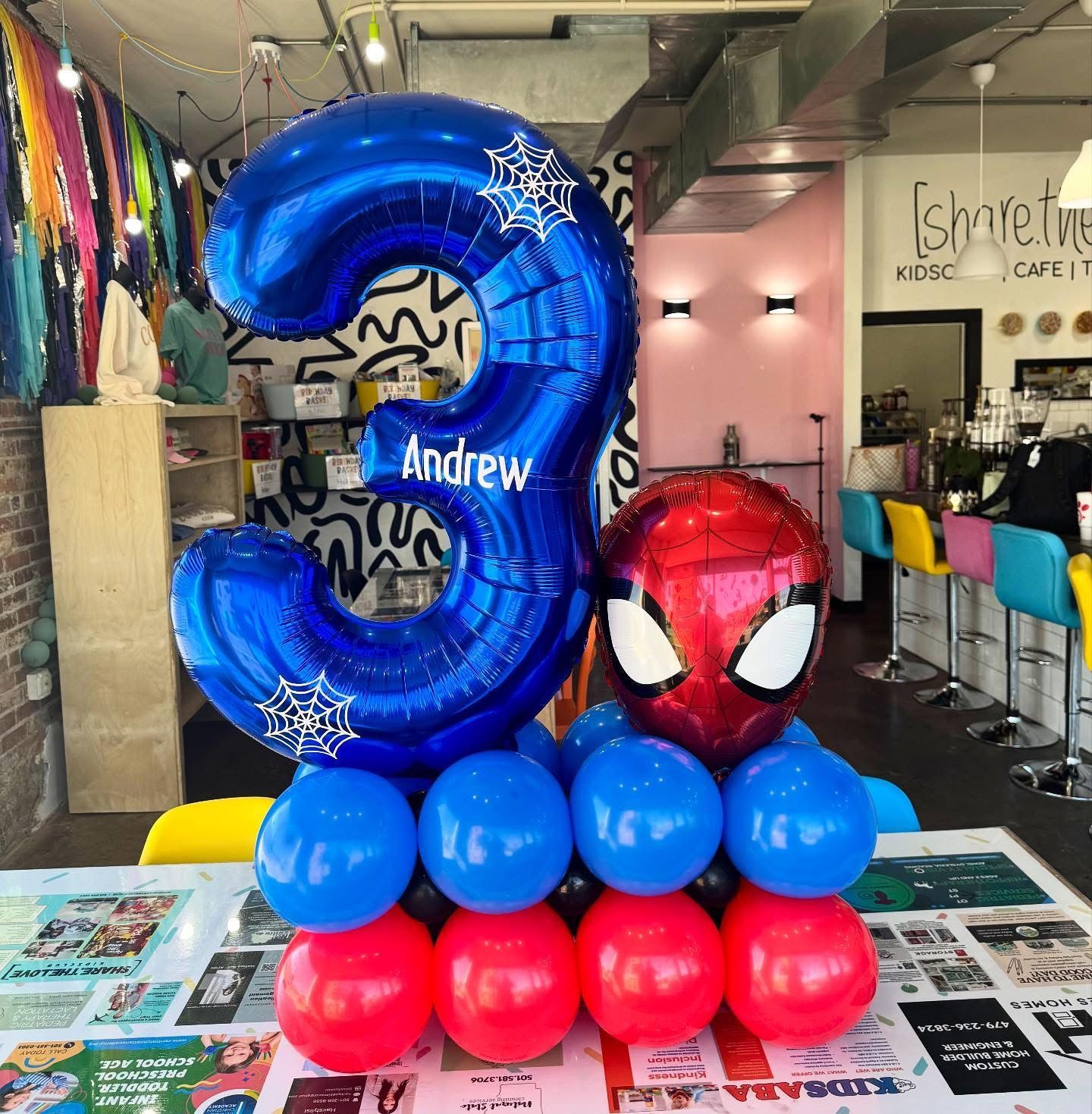 Spider-Man and blue balloon number 3 with Andrew in a colorful storefront display
