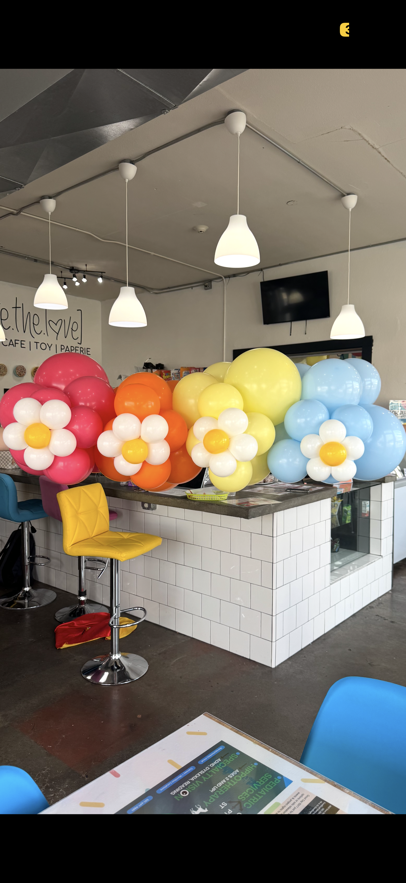 Colorful balloon garlands decorate a café counter with white tiles and hanging pendant lights.