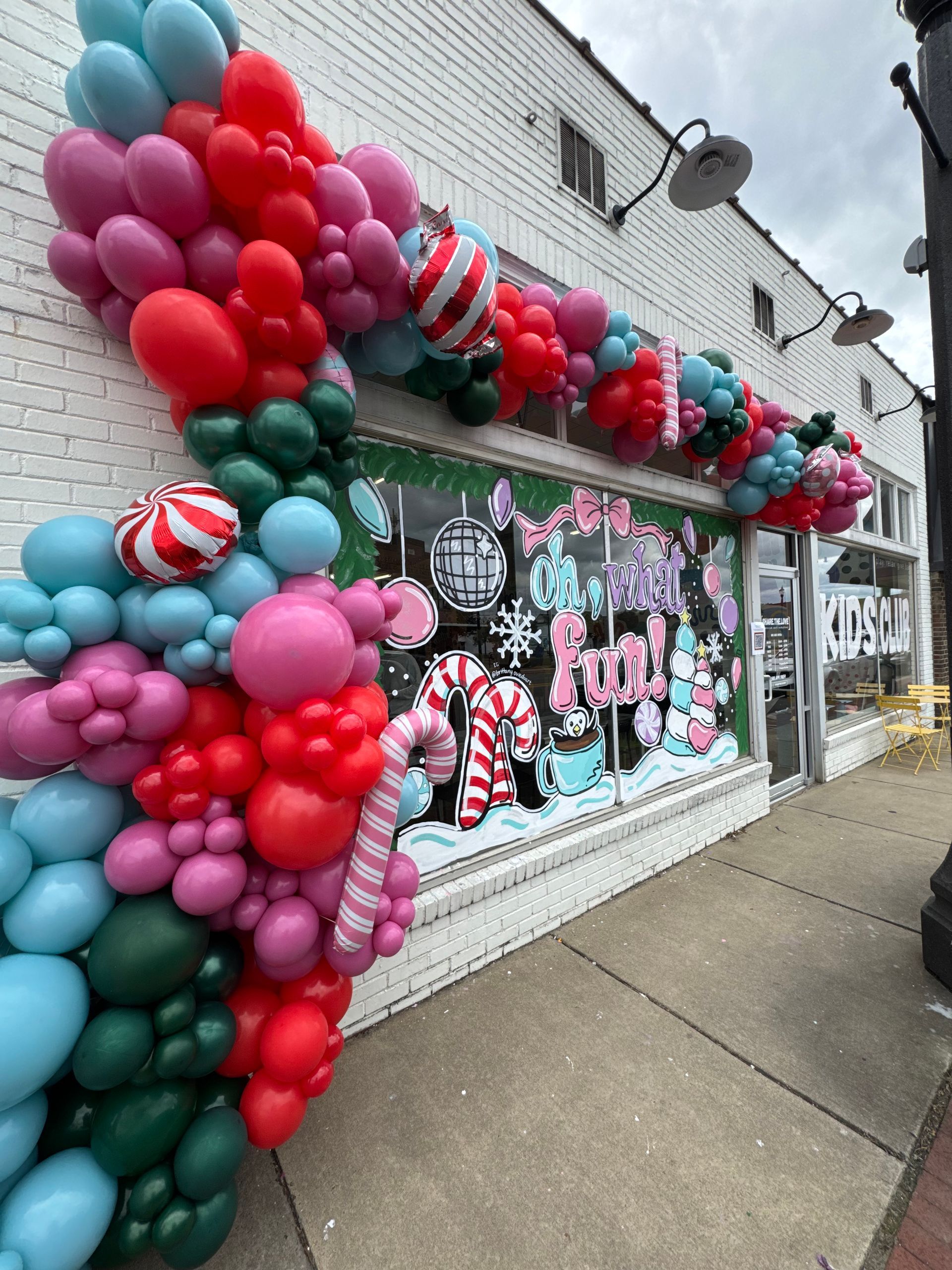 Balloon-decorated storefront with colorful pink, red, teal, and mint holiday window display