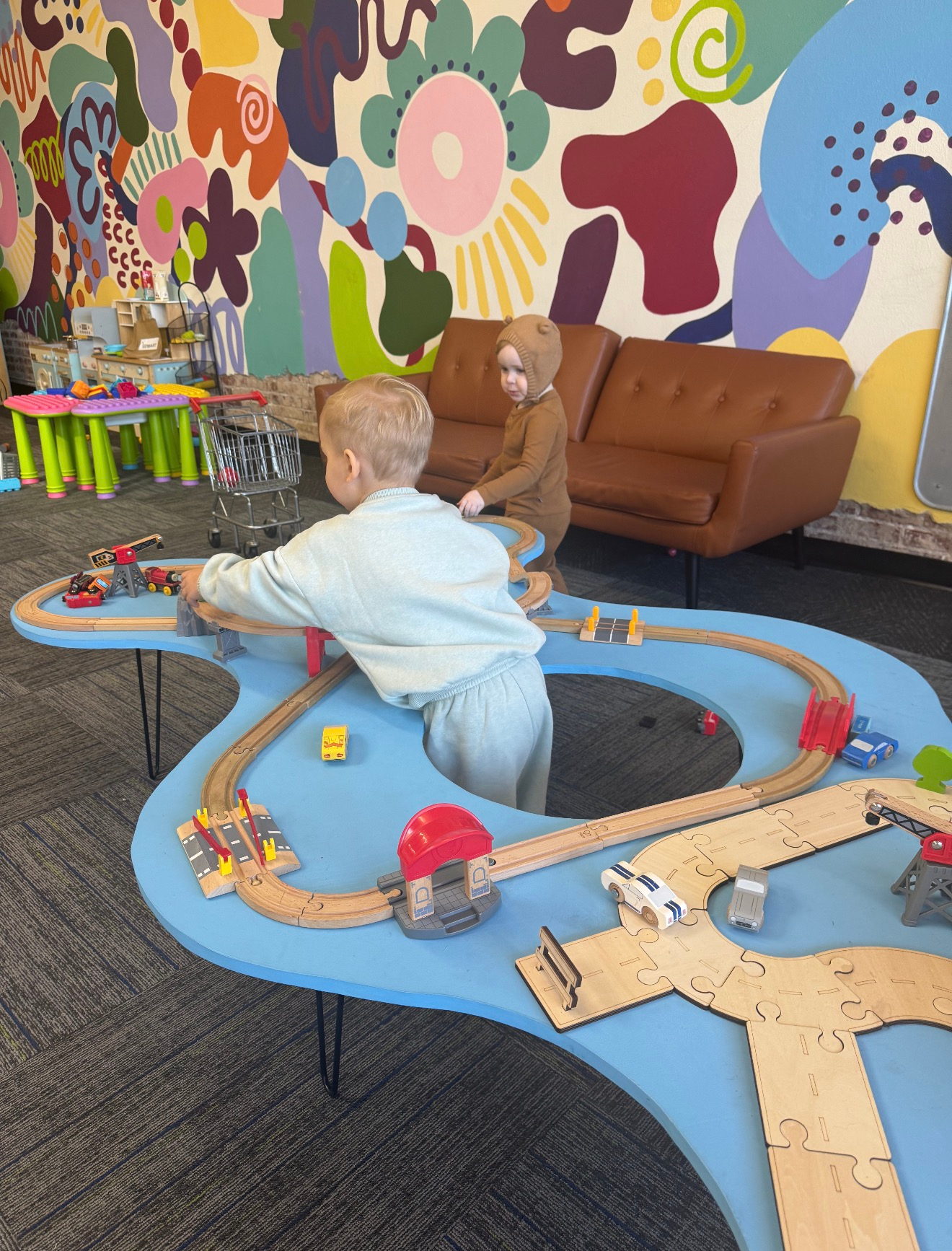 Children playing with toy trains on a blue carpet in a colorful indoor play area