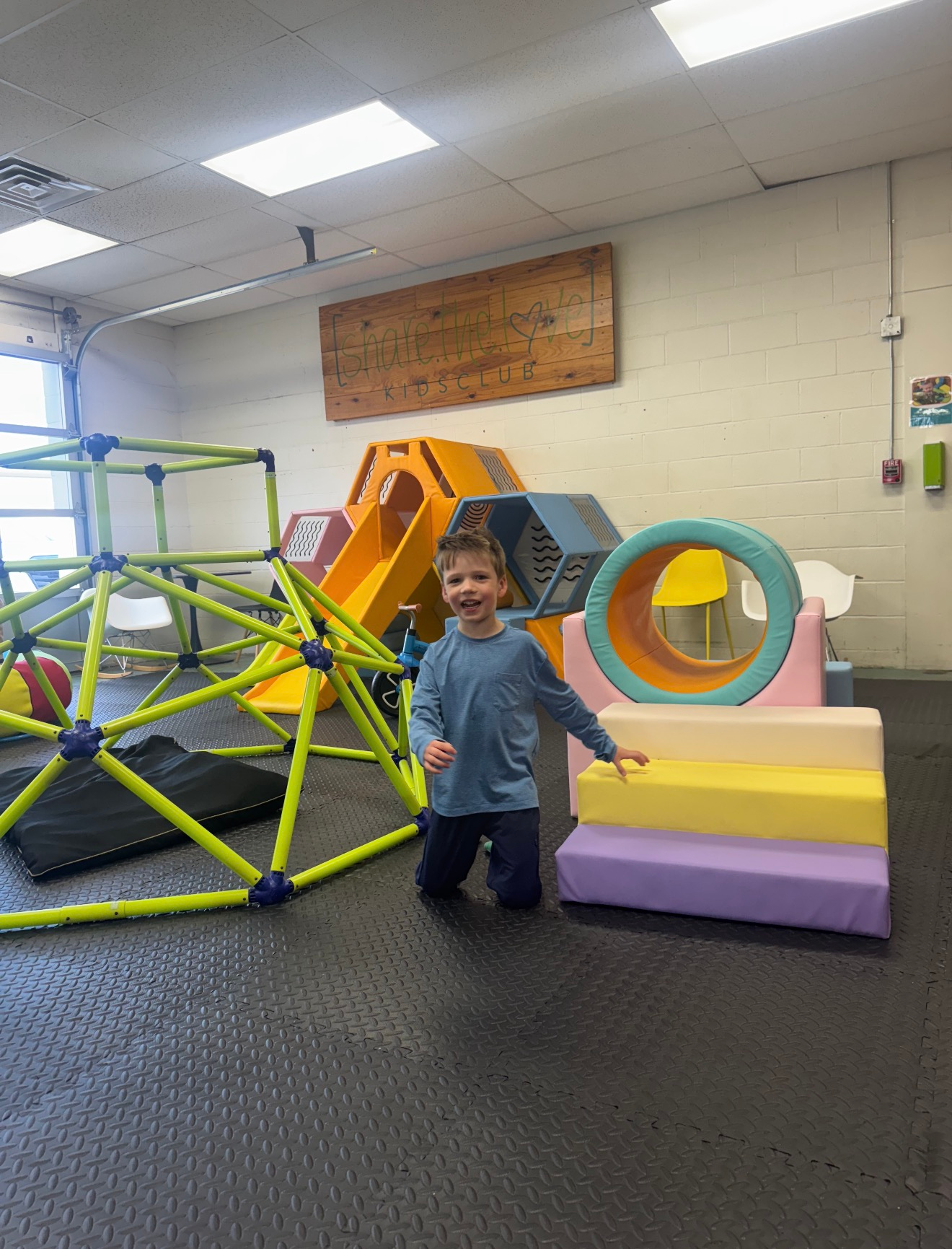 Child smiling in an indoor playroom beside colorful climbing blocks and tunnel equipment