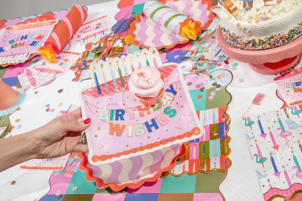 Colorful birthday party table with a hand holding a “Best Wishes” gift box and a cupcake centerpiece