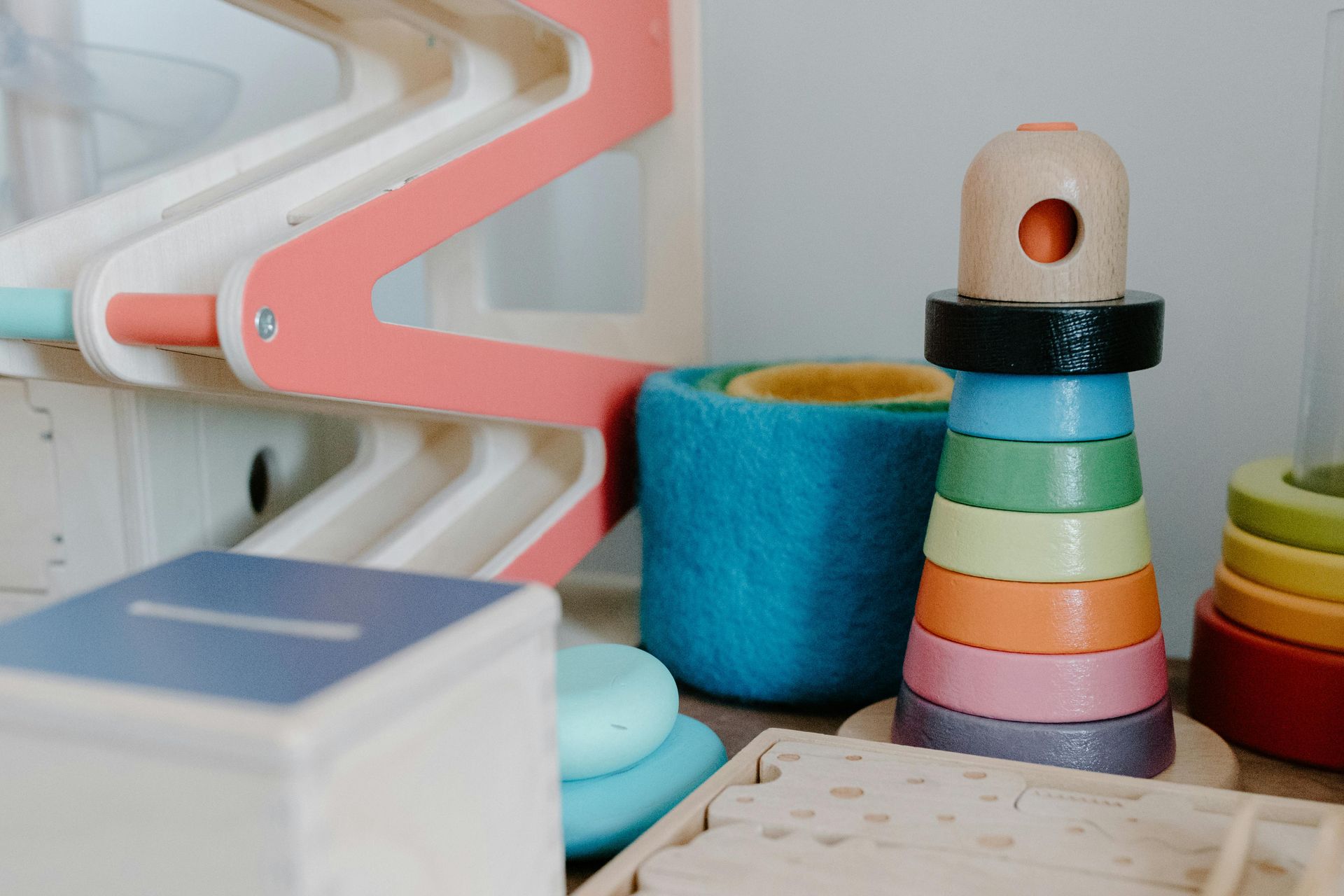 Colorful wooden toys and blocks on a shelf, including stacking rings, a blue cylinder, and a white cube