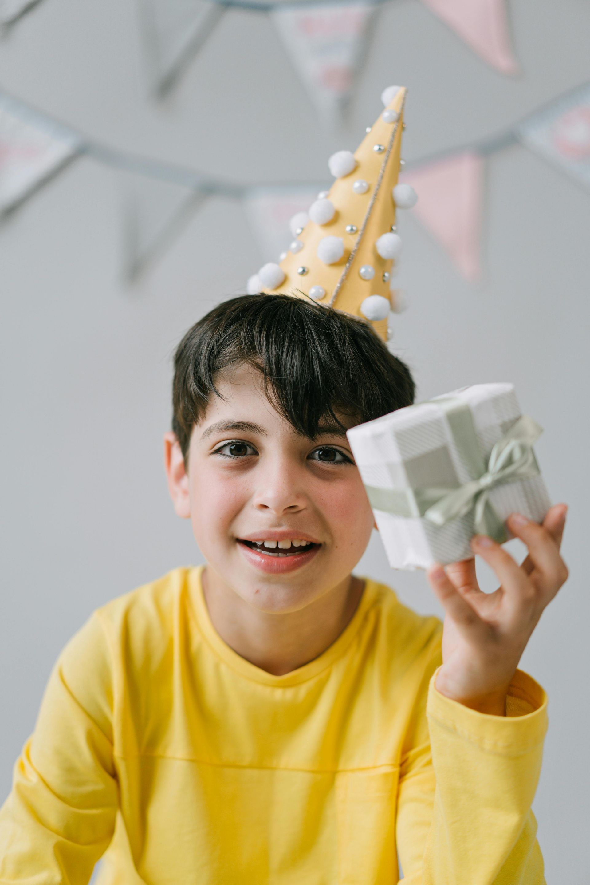 Smiling child in yellow shirt holding a gift and wearing a party hat.