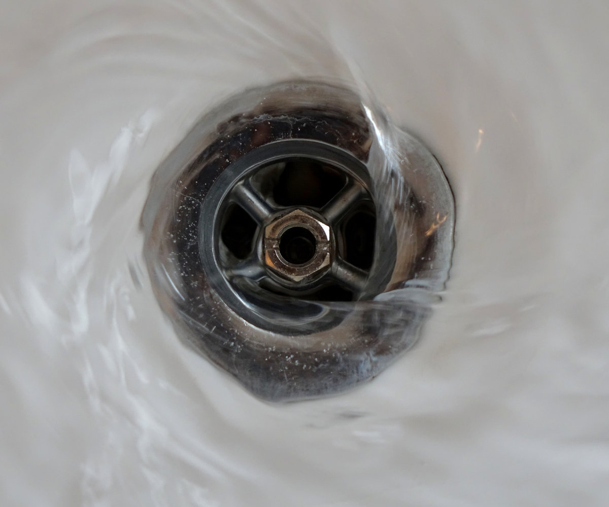 Water swirling down a chrome drain in a white sink.