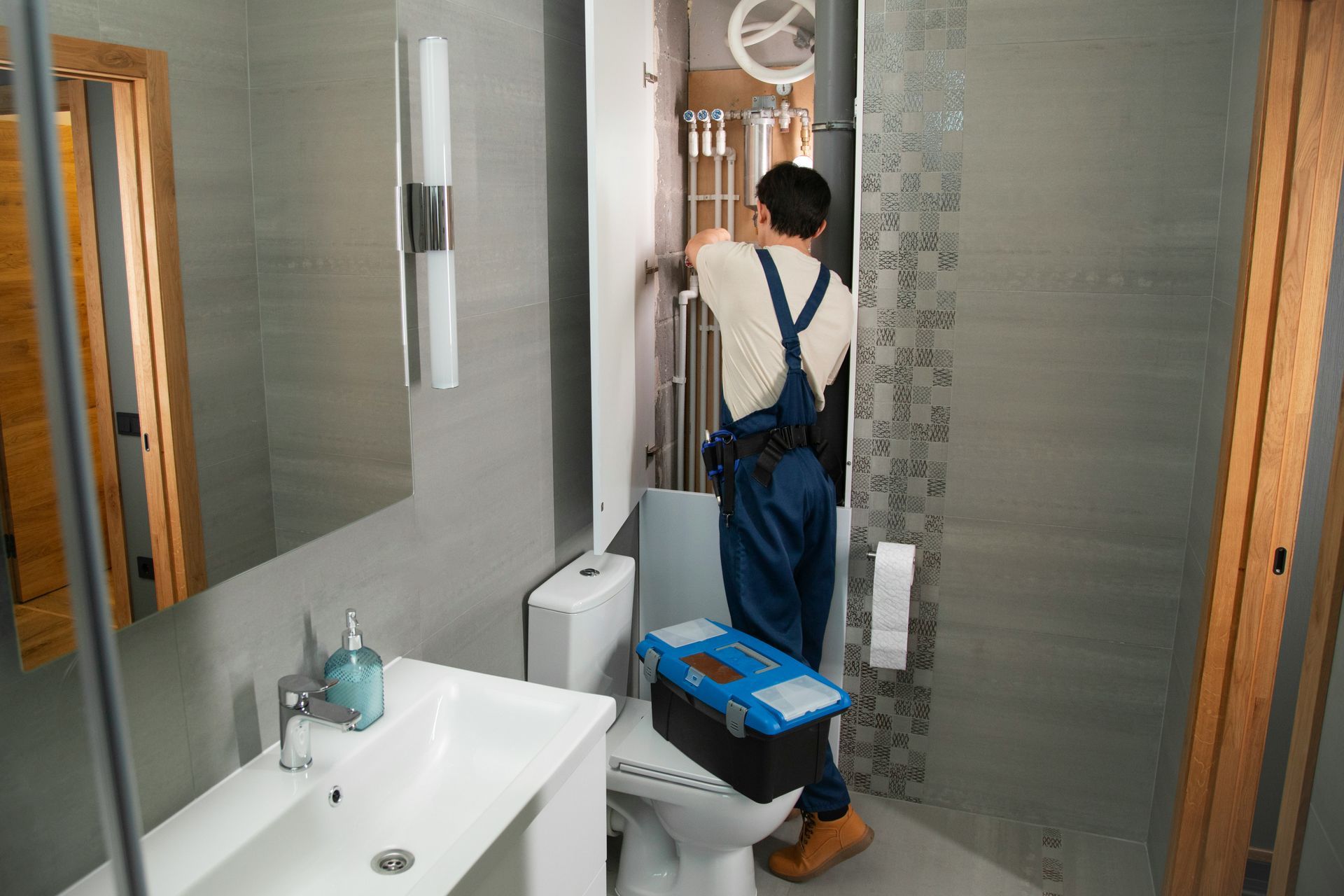 Plumber in blue overalls repairing a bathroom fixture, standing on the toilet.