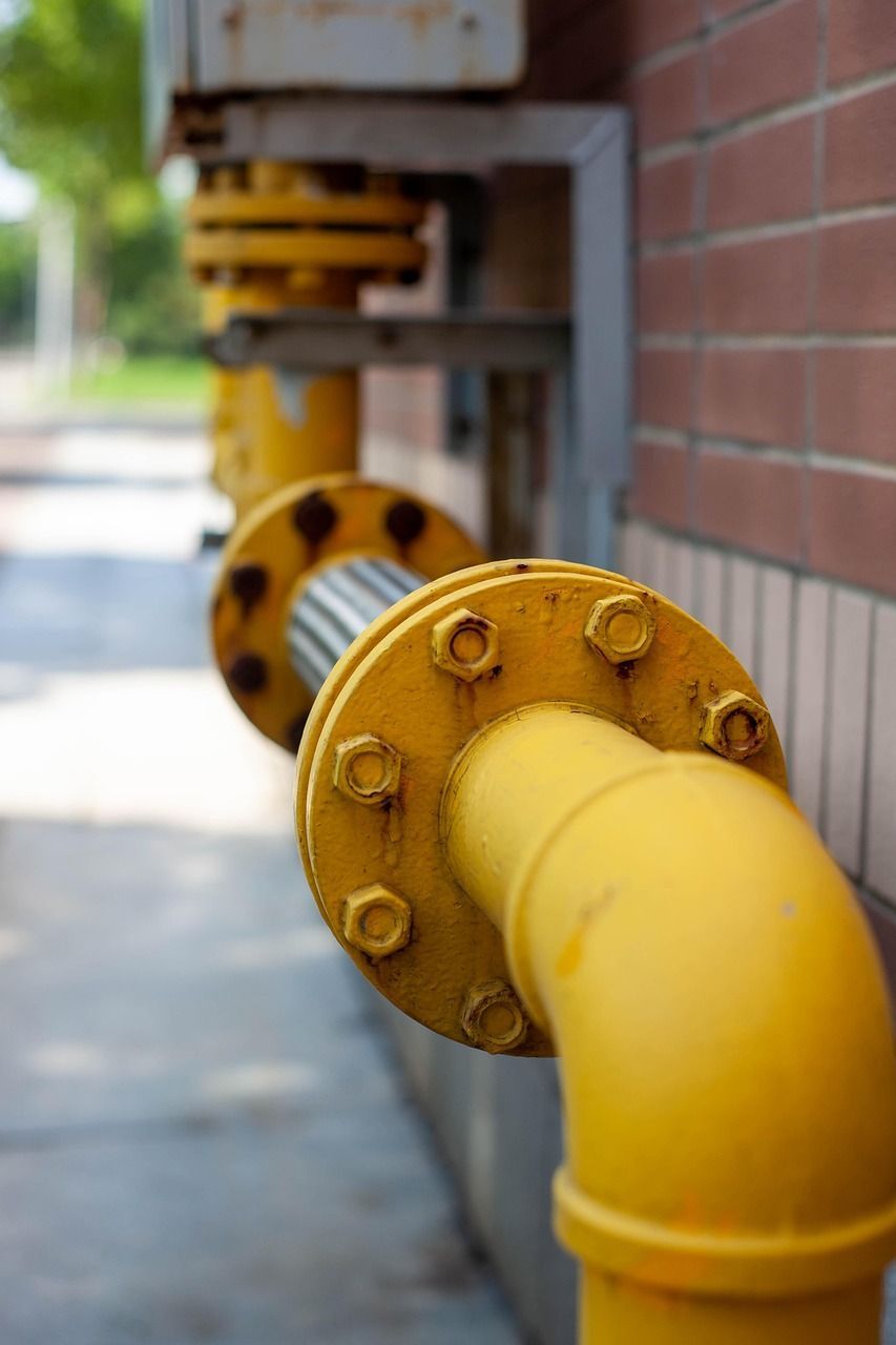 Yellow gas pipes with bolted flanges on a brick building.