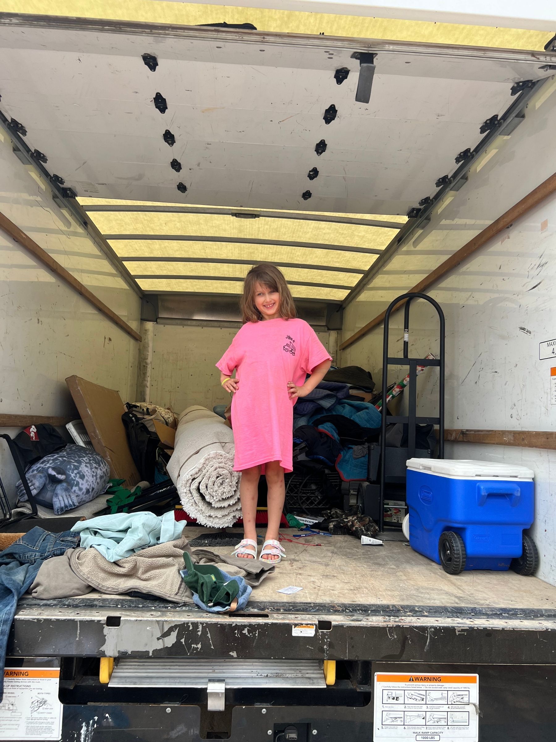 A little girl is standing in the back of a moving truck.