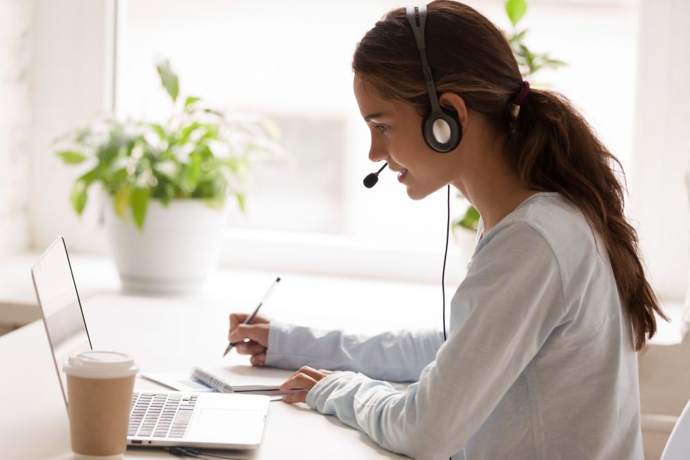 Woman Wearing a Headset Working on a Laptop and Taking Notes at a Desk — Clarity Family Therapy in Brisbane, QLD