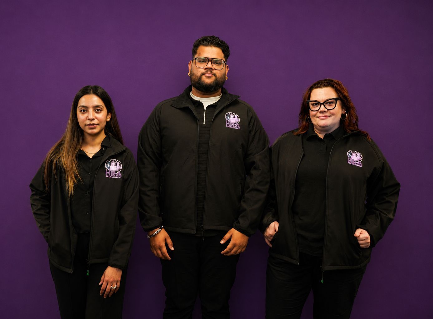 Three people in black jackets standing against a purple backdrop