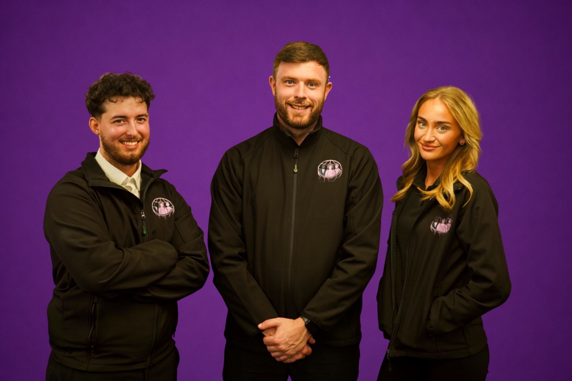 Three people in black jackets posing against a purple background.