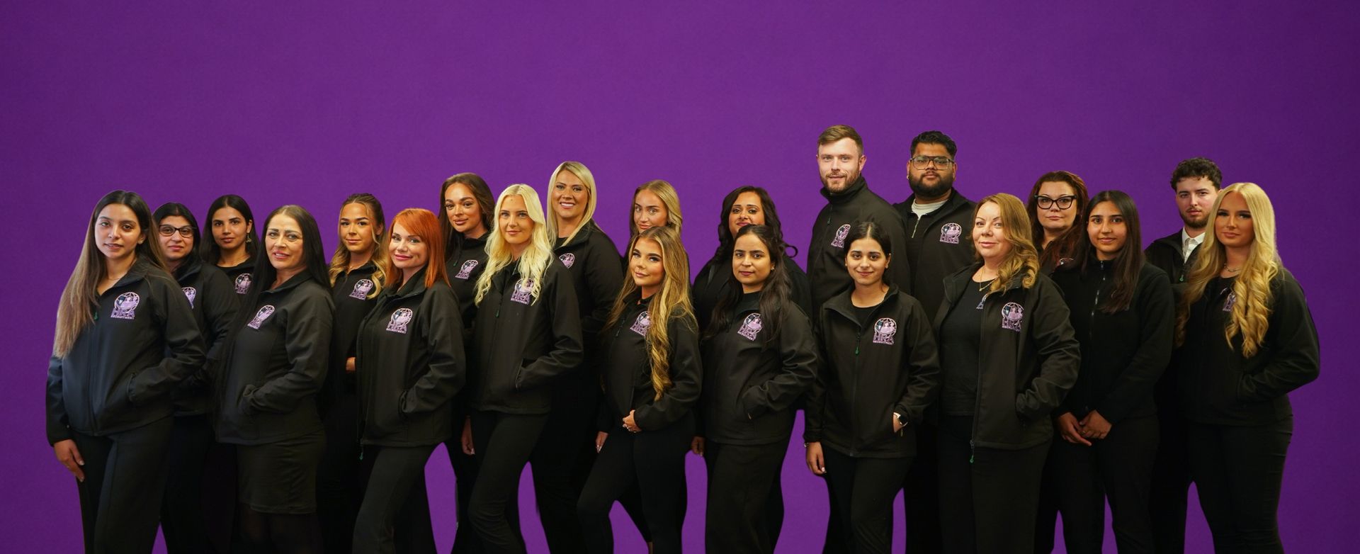 Group of people in black suits standing on a purple-lit stage against a purple background