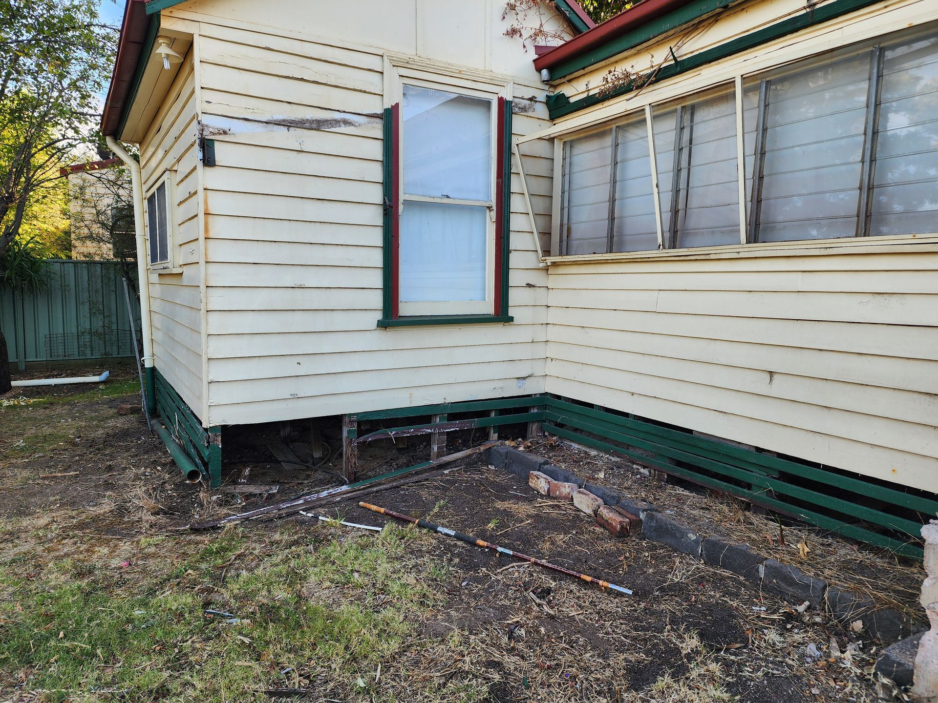Side of a white house with peeling siding, small window, and bare yard with dirt and debris