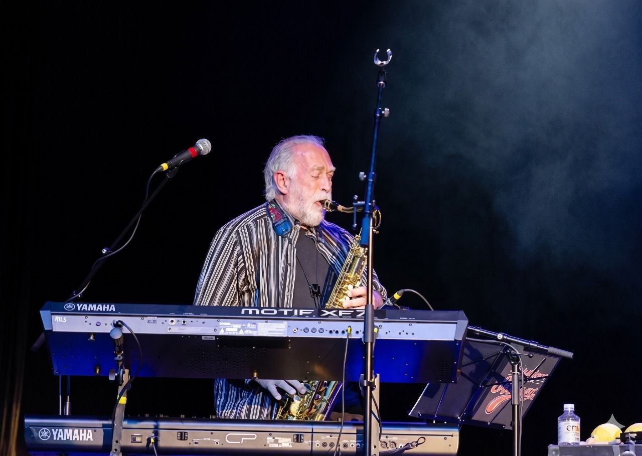 Musician at a keyboard and microphone on a dark stage, singing under blue lights.