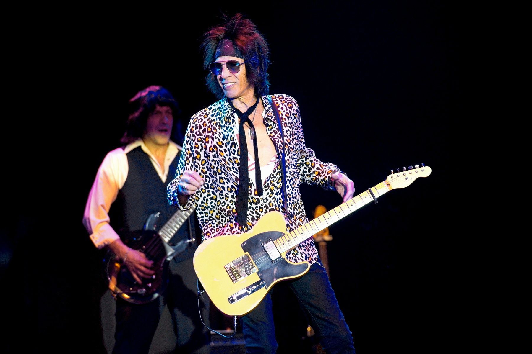 Two musicians performing onstage, one playing a yellow electric guitar under dark lighting