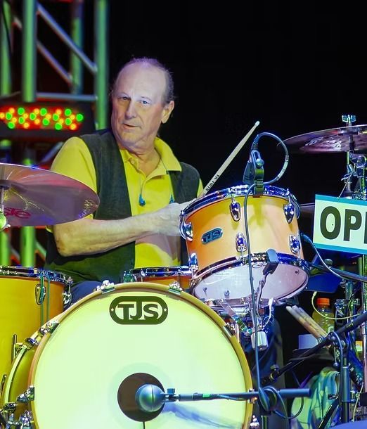 Drummer in a yellow shirt playing a yellow drum kit on stage under colored lights
