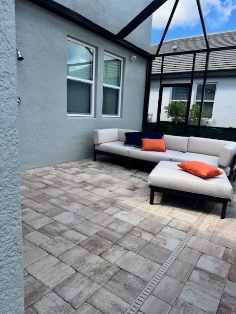 Modern patio with gray pavers, white outdoor sofa, and orange cushions under a covered pergola.