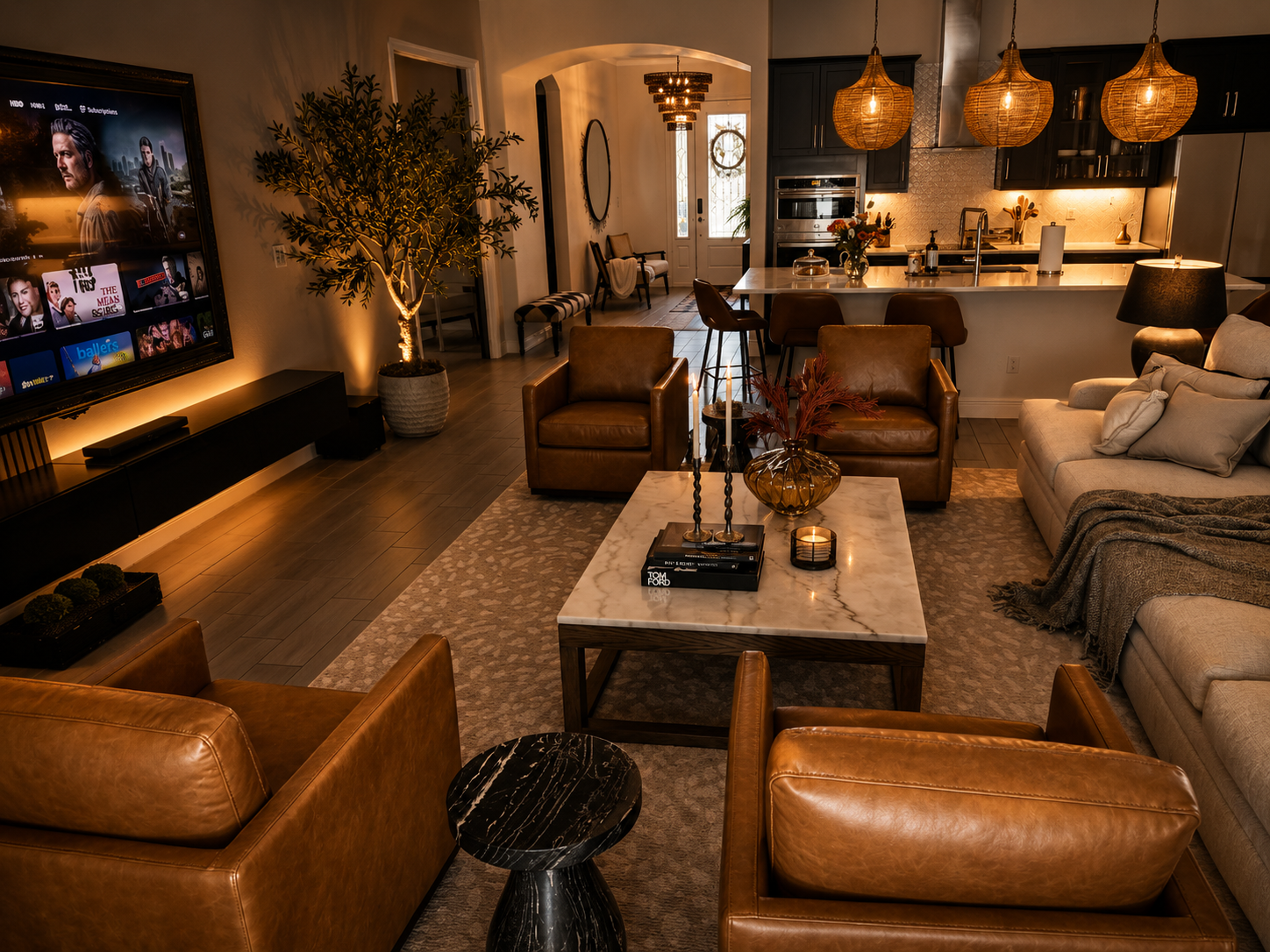 Cozy modern living room with leather chairs, sectional sofa, warm lighting, and a wall-mounted TV