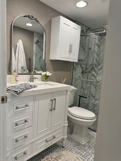 Small gray bathroom with white vanity, sink, mirror, toilet, and glass shower.