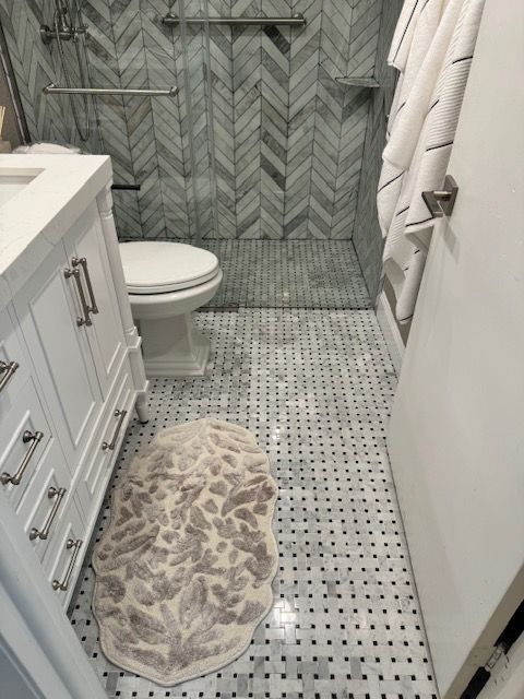Narrow bathroom with white vanity, toilet, gray chevron shower wall, and patterned tile floor.