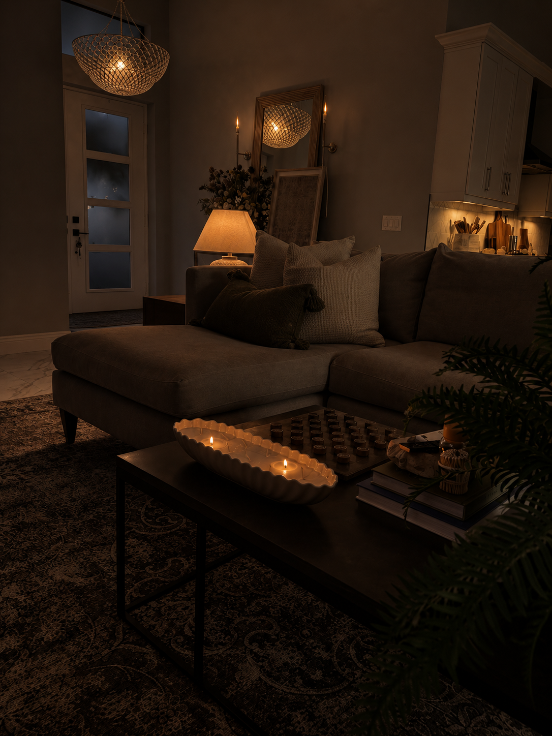 Dim living room with warm lamps, sectional sofa, coffee table, and candlelight on a patterned rug.