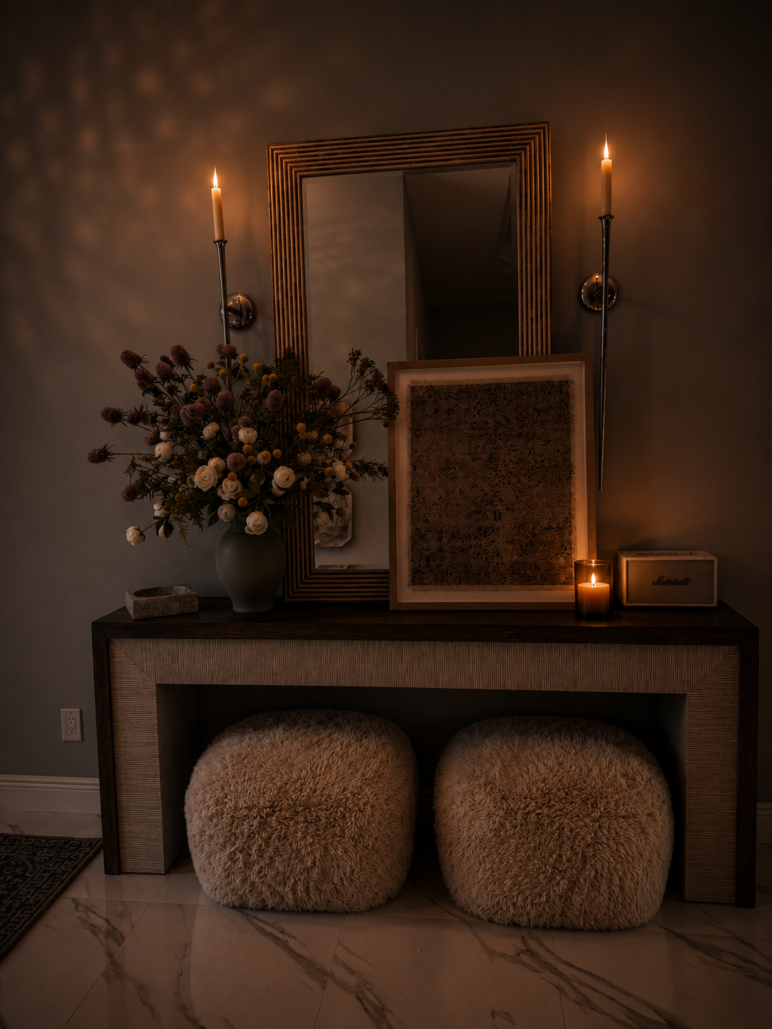 Dimly lit mantel with candles, framed art, a floral arrangement, and two woven poufs below
