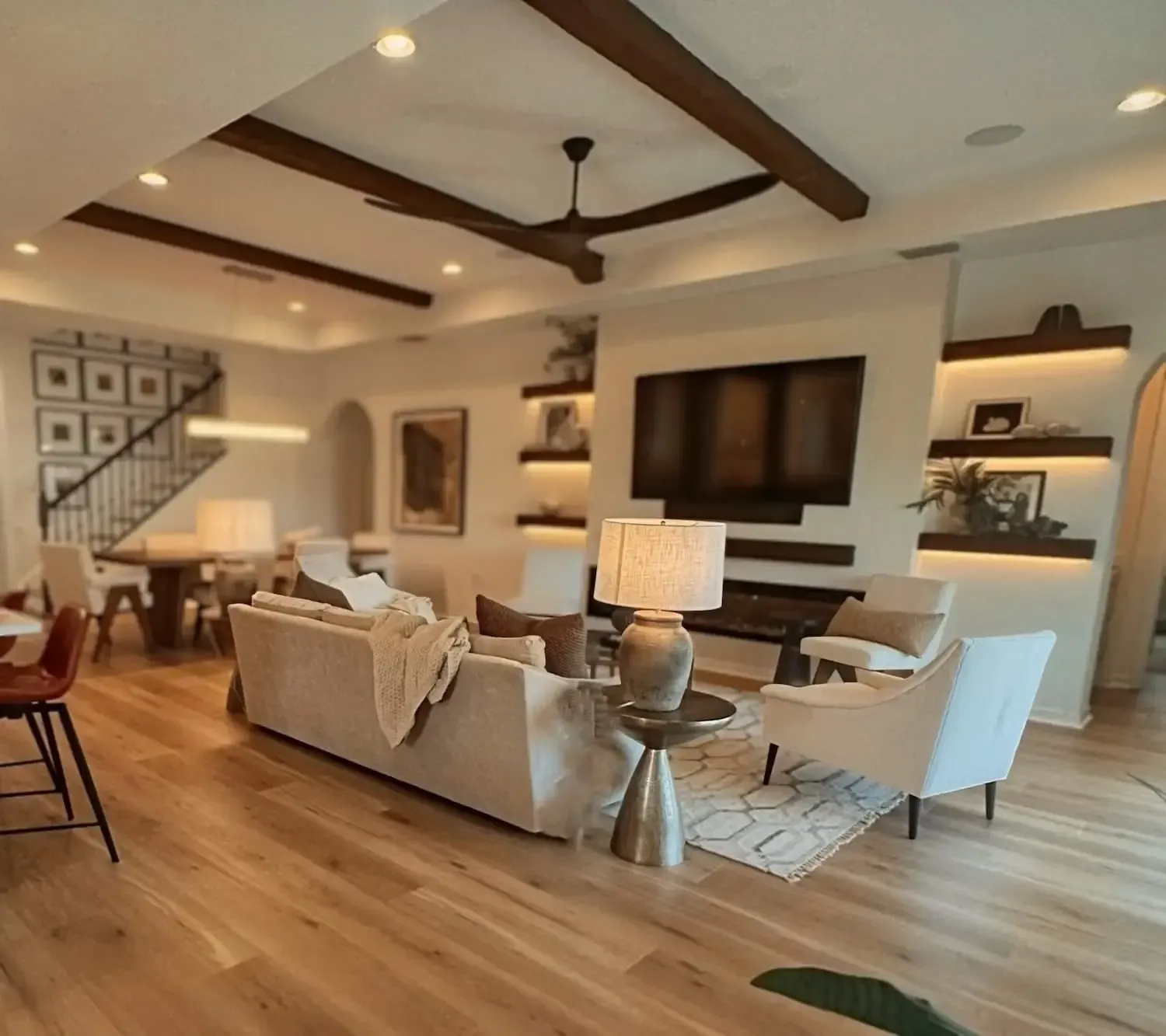 Bright modern living room with beige sofas, wall-mounted TV, wood beams, and warm lighting